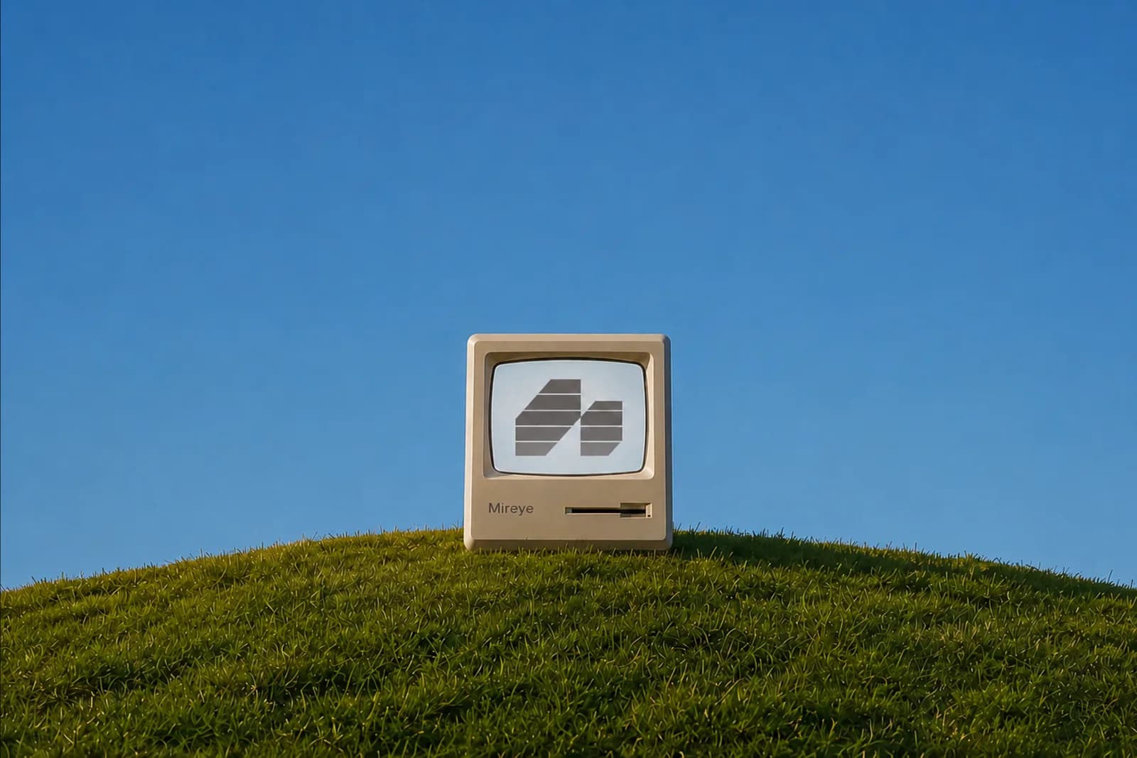 The Mireye mark on the screen of a vintage desktop computer, standing on a grassy hill under a clear sky